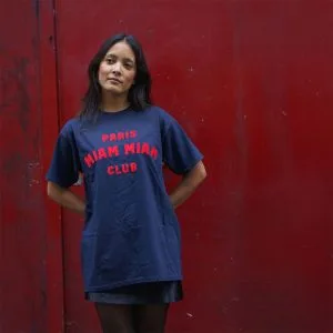 Model wearing a navy blue Paris Miam Miam Club T-shirt in front of a red door