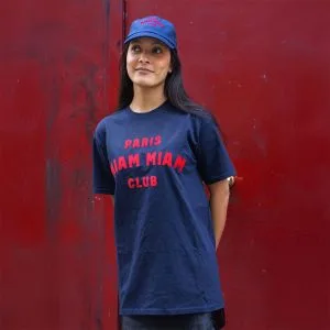 Model wearing a navy blue Paris Miam Miam Club T-shirt and cap in front of a red door